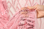 A hand is holding a pink sequin fabric, with the fabric's intricate patterns and textures visible.