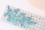 a close-up view of a decorative blue and silver lace piece, with a ruler placed on top of it.