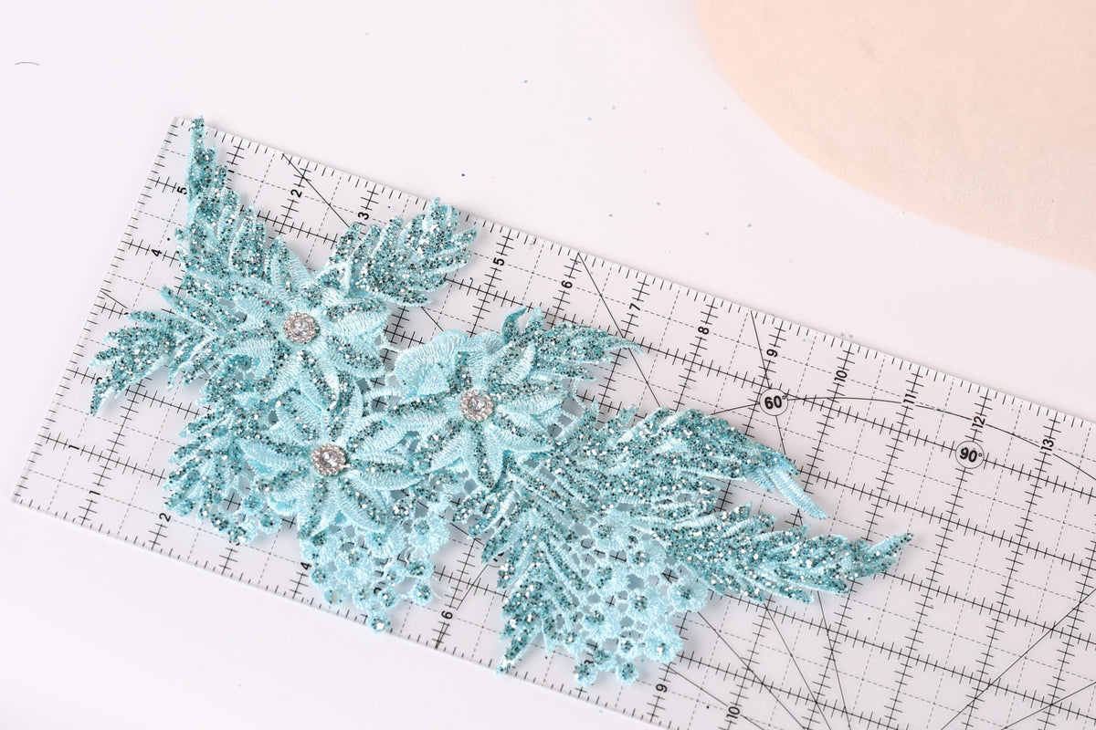 a close-up view of a decorative blue and silver lace piece, with a ruler placed on top of it.