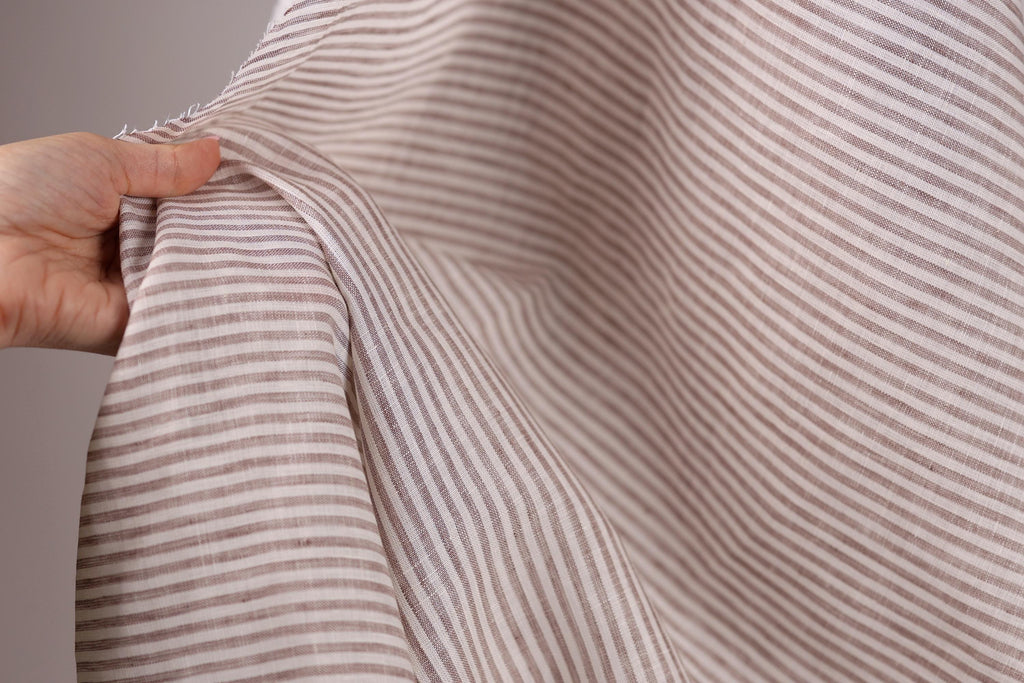 A hand is holding a piece of fabric with a striped pattern, which appears to be a light brown color.