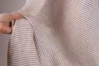 A hand is holding a piece of fabric with a striped pattern, which appears to be a light brown color.