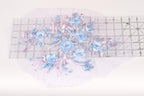 a delicate floral arrangement with blue flowers and beaded accents, placed on a transparent surface.