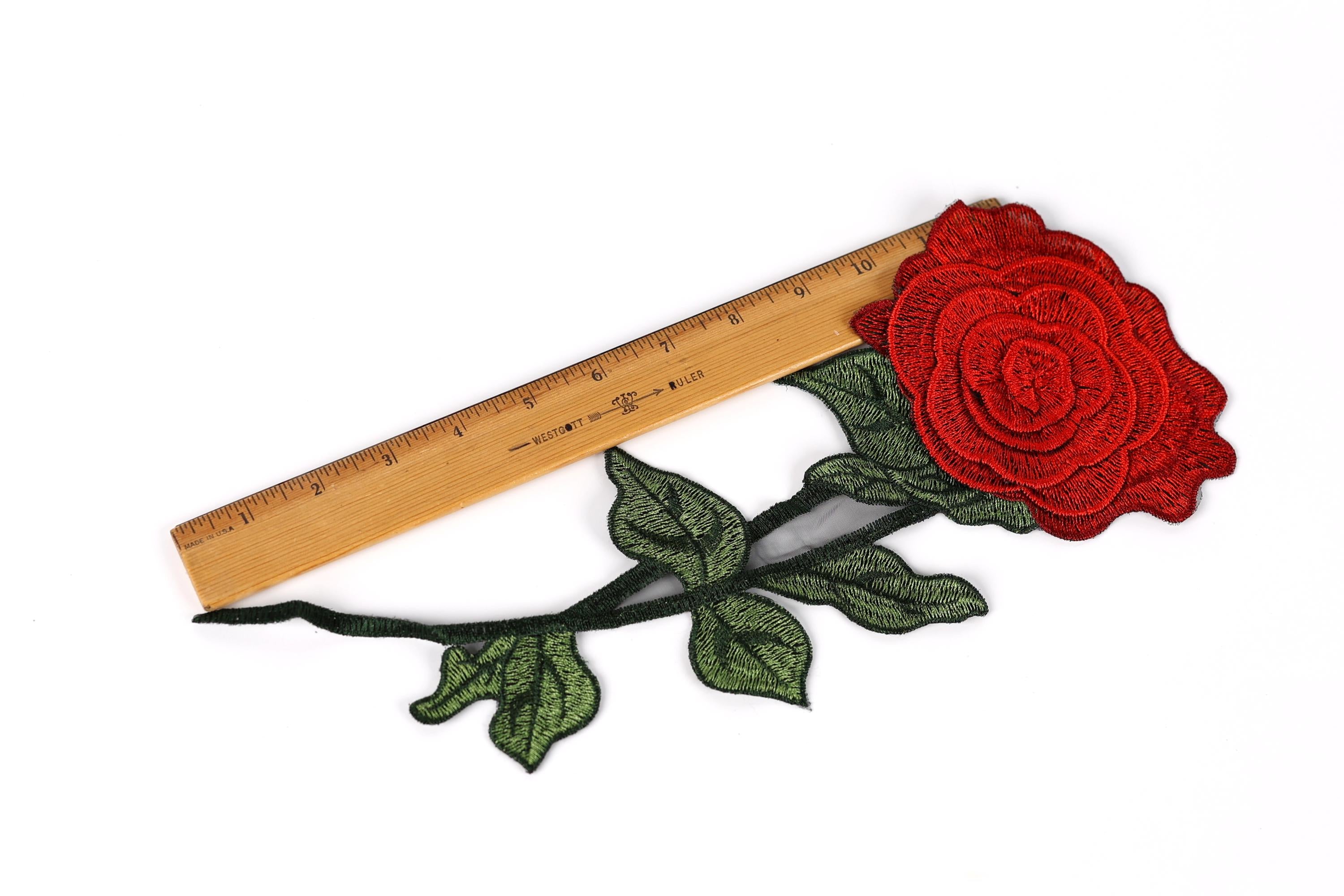 a red rose embroidered on a branch, with a wooden ruler placed next to it.