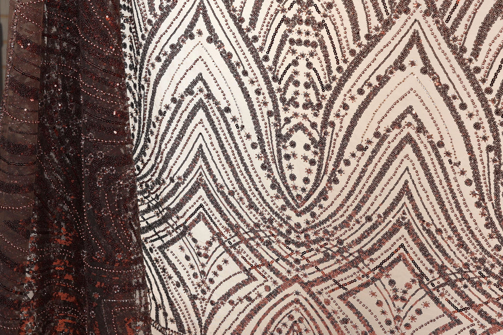 a close-up view of a fabric with a pattern of brown and white sequins and lines. The fabric appears to be a sheer material, with a textured and ornate design.