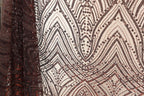 a close-up view of a fabric with a pattern of brown and white sequins and lines. The fabric appears to be a sheer material, with a textured and ornate design.