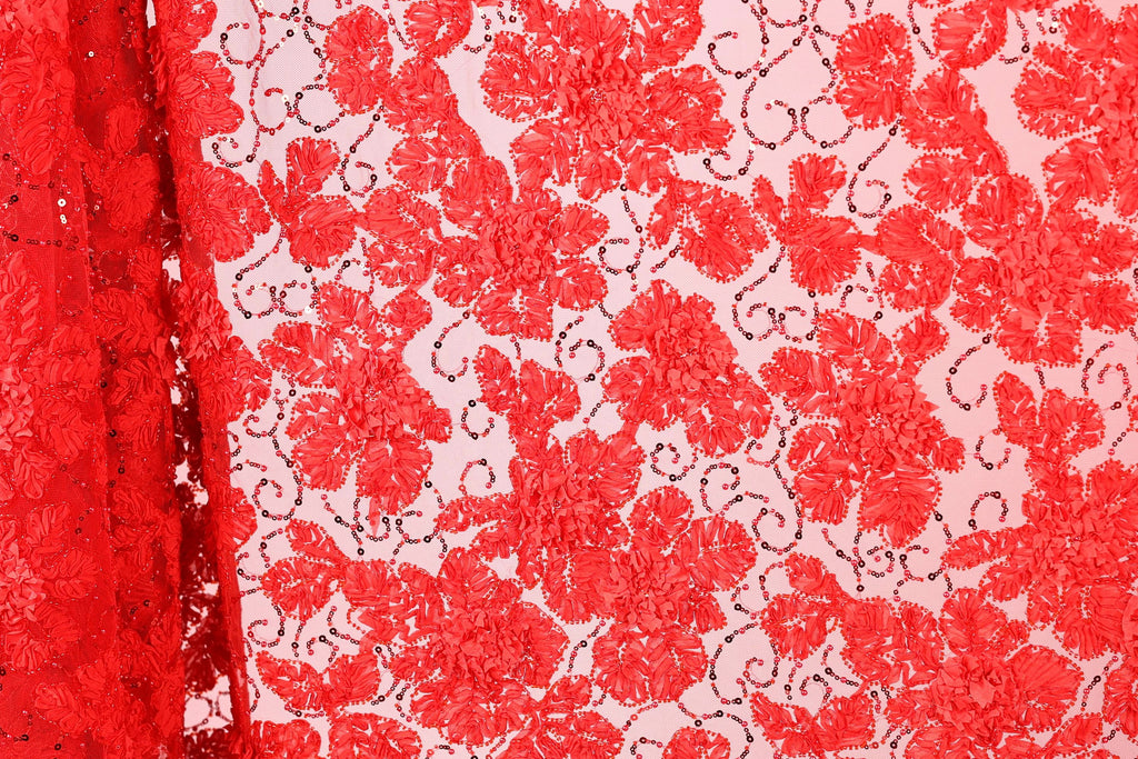 a close-up view of a red fabric with a floral pattern. The fabric appears to be made of a sheer material, with a repeating pattern of red flowers and leaves. The fabric is displayed in a vertical orientation, with the left side of the fabric partially visible.