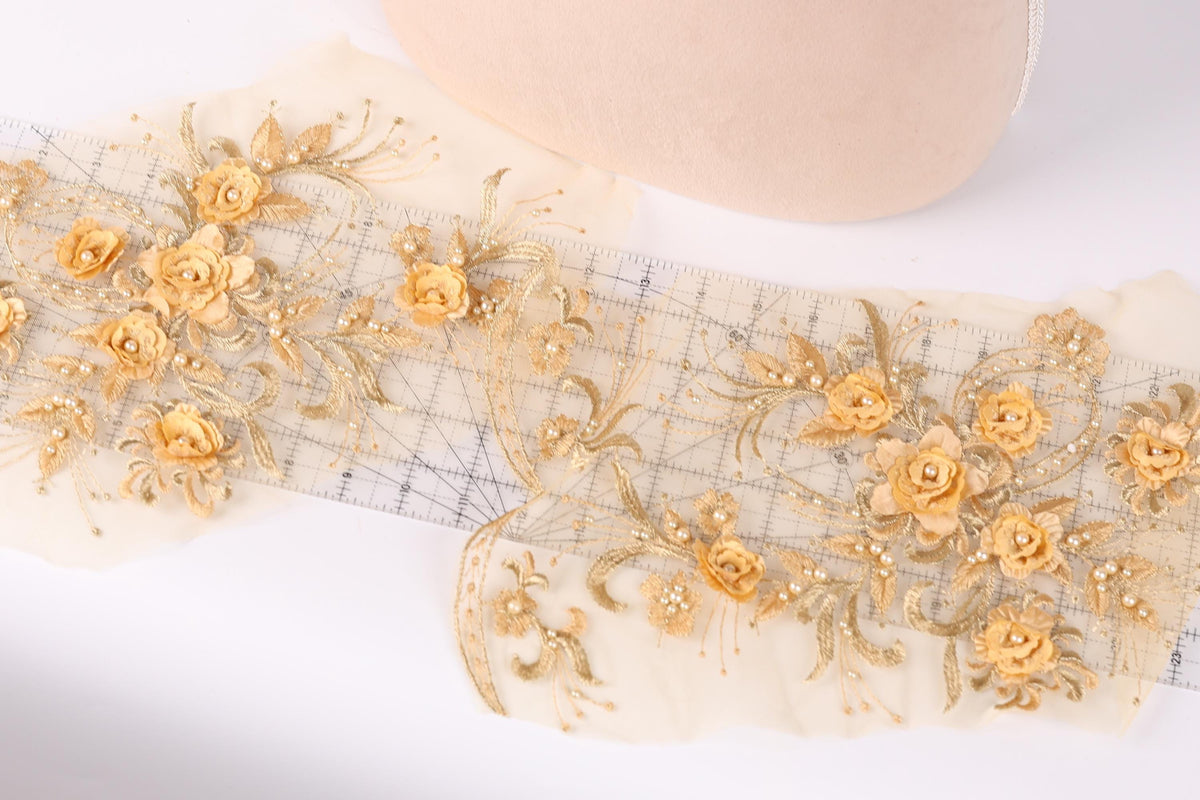 a close-up view of a delicate, ornate fabric with a floral pattern. The fabric is adorned with numerous small gold flowers, creating a visually striking and intricate design. The flowers are arranged in a way that they appear to be growing out of the fabric, adding a sense of depth and dimension to the piece. The fabric is spread out on a white surface, allowing the viewer to appreciate the intricate details and craftsmanship of the design.