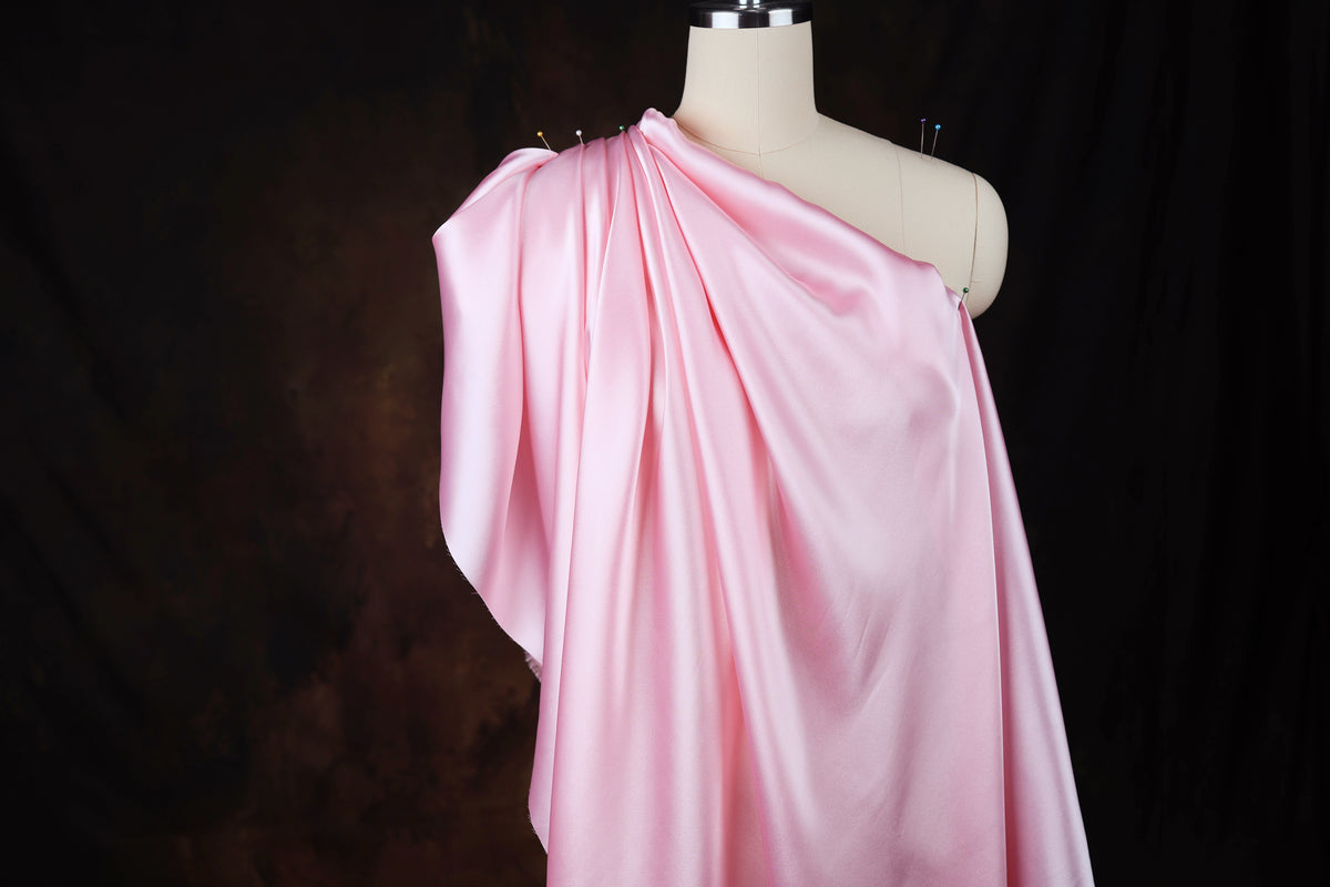A mannequin wearing a pink satin dress with a draped, flowing silhouette.