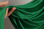 A hand with painted fingernails is holding a green fabric, which appears to be a soft, flowing material.