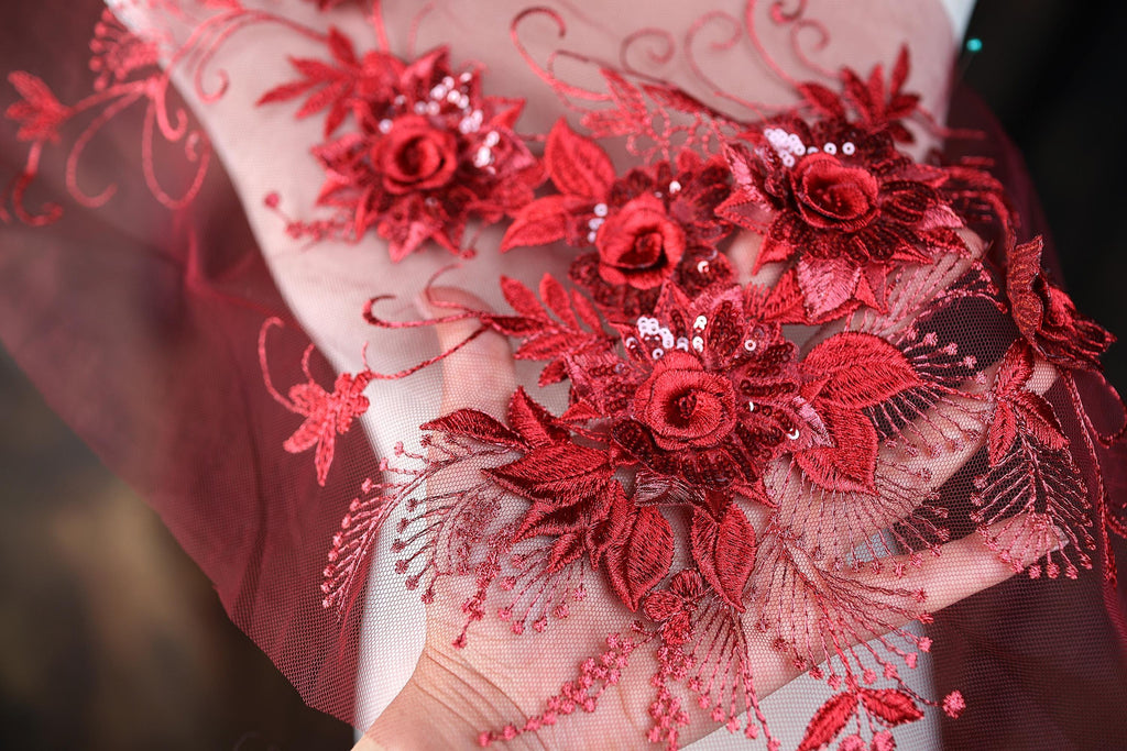 a close-up view of a hand holding a piece of red lace with intricate floral embroidery.