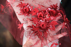 a close-up view of a hand holding a piece of red lace with intricate floral embroidery.