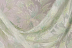 a close-up view of a delicate, light green fabric with a floral pattern. The fabric appears to be made of sheer material, with small, colorful beads or sequins scattered throughout the design. The overall composition of the image is visually appealing and showcases the intricate details of the fabric.