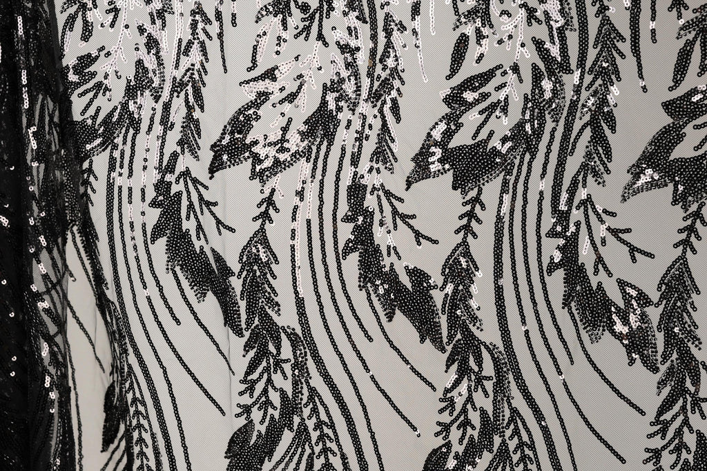 a close-up view of a black and white fabric with a repeating pattern of sequin designs. The pattern consists of various shapes and lines, creating a visually striking and intricate design. The fabric appears to be made of a material that resembles lace or sheer fabric, with the sequins adding a touch of sparkle and texture to the overall appearance.