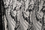 a close-up view of a black and white fabric with a repeating pattern of sequin designs. The pattern consists of various shapes and lines, creating a visually striking and intricate design. The fabric appears to be made of a material that resembles lace or sheer fabric, with the sequins adding a touch of sparkle and texture to the overall appearance.