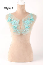 A mannequin with a light-colored fabric draped over it, featuring intricate floral embroidery in a light blue color.