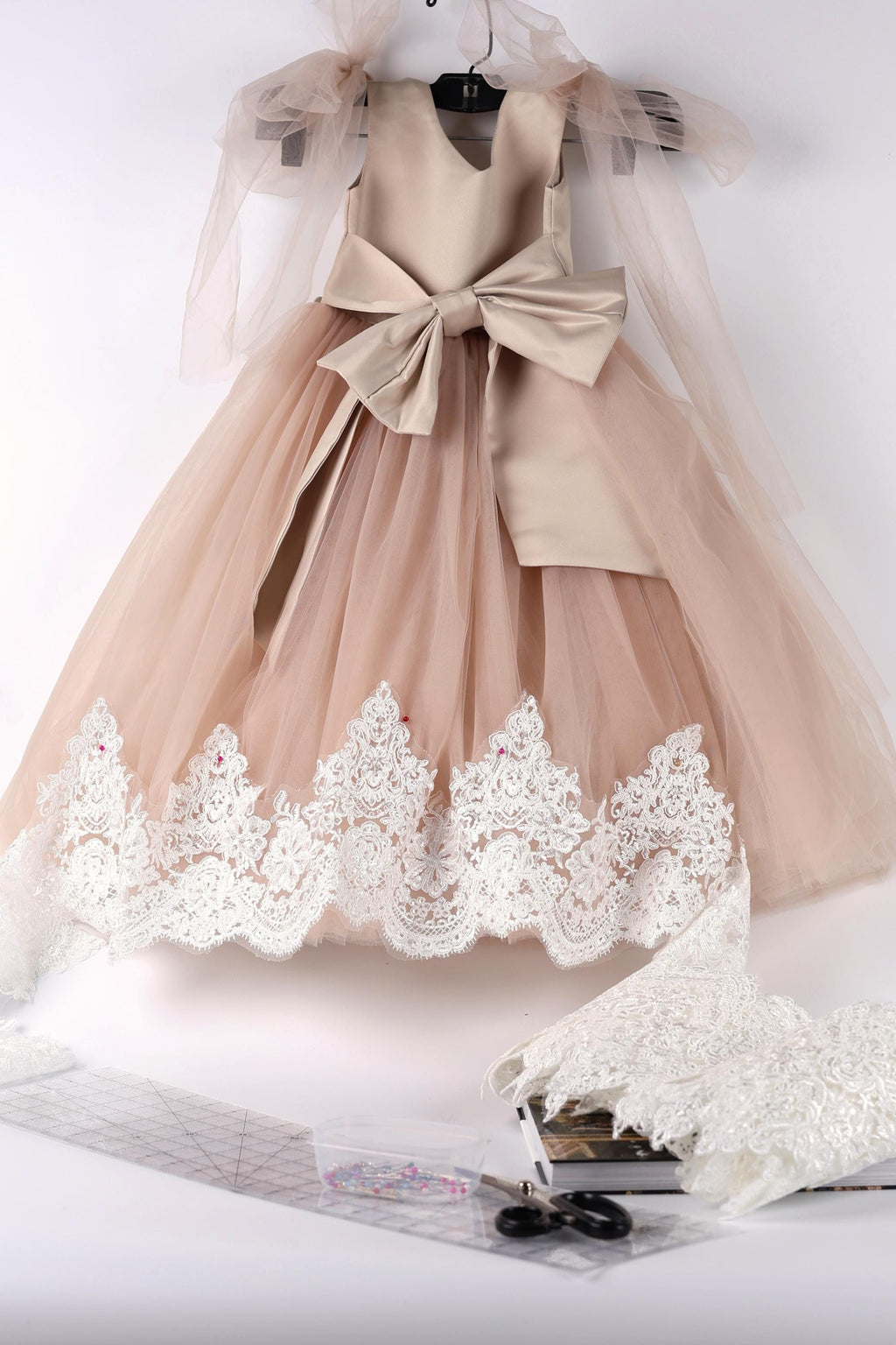 A beige dress with a bow and lace trim, hanging on a hanger against a white background.