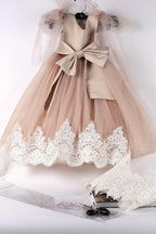 A beige dress with a bow and lace trim, hanging on a hanger against a white background.