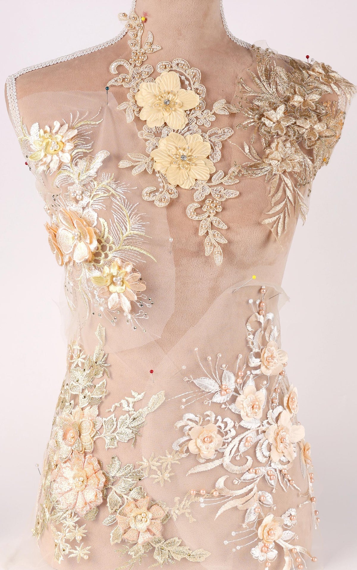 A mannequin torso covered in intricate, delicate embroidered floral designs in various shades of yellow and beige.