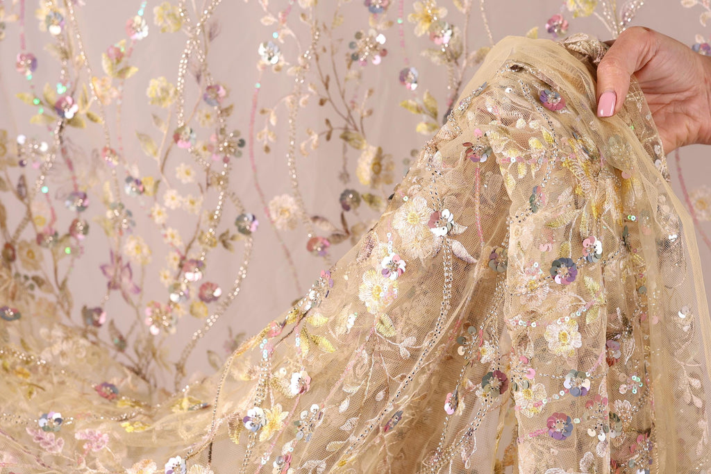 A hand is holding a piece of fabric with a floral pattern, featuring a mix of pink, yellow, and white colors.