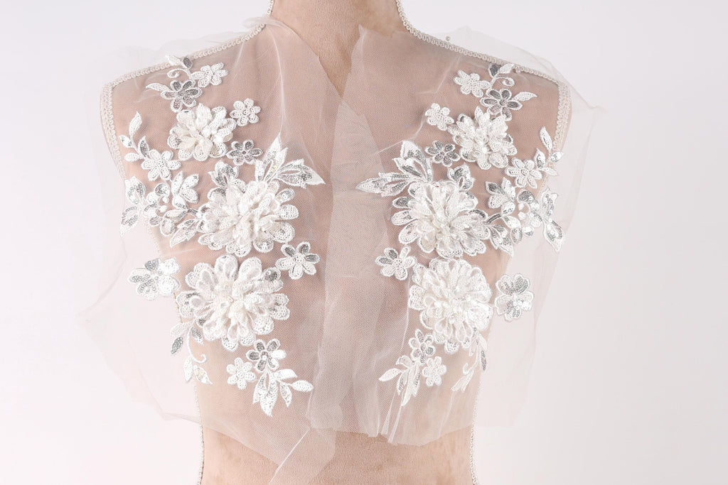 A mannequin wearing a white lace dress with intricate floral embroidery on the shoulders and back.
