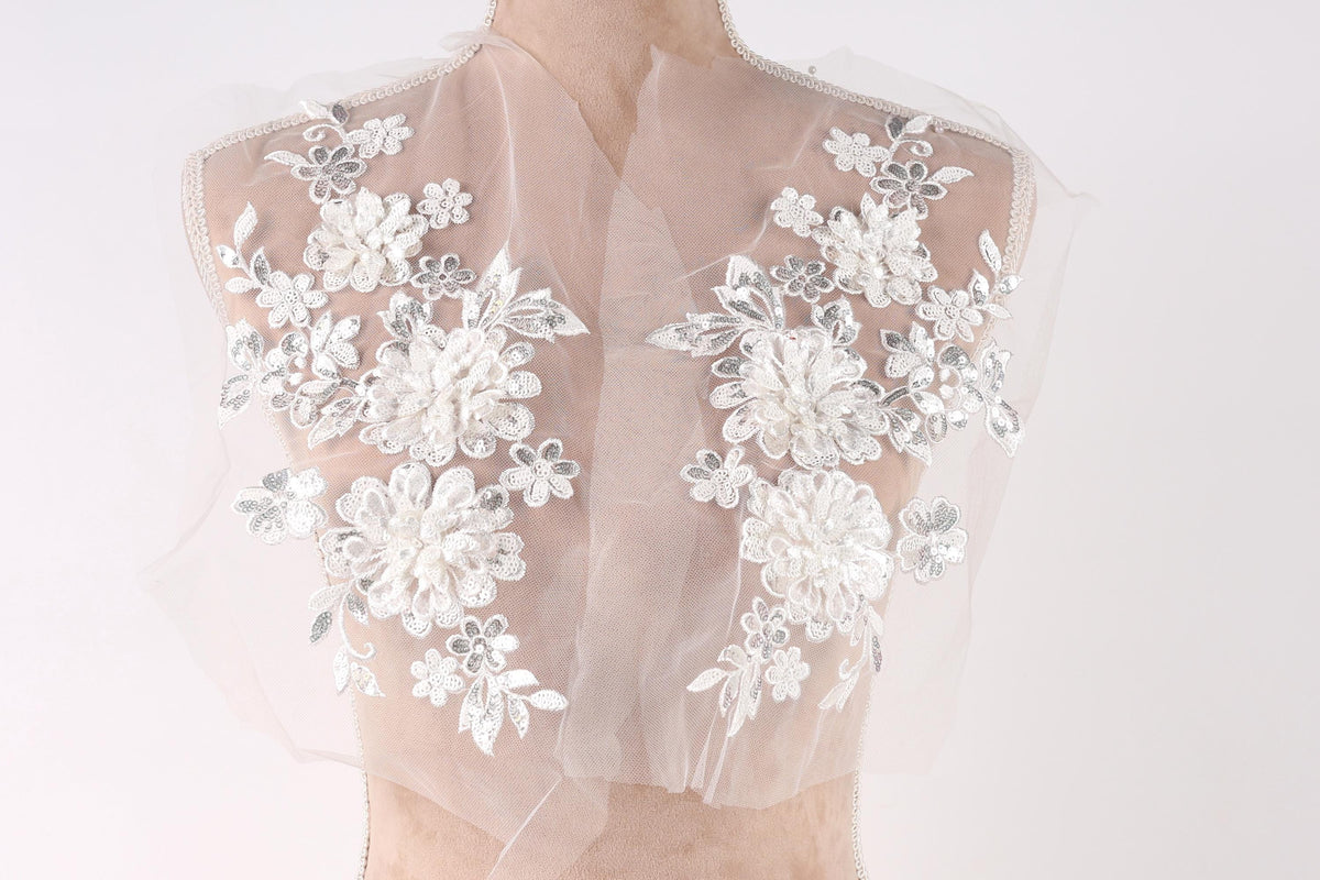 A mannequin wearing a white lace dress with intricate floral embroidery on the shoulders and back.