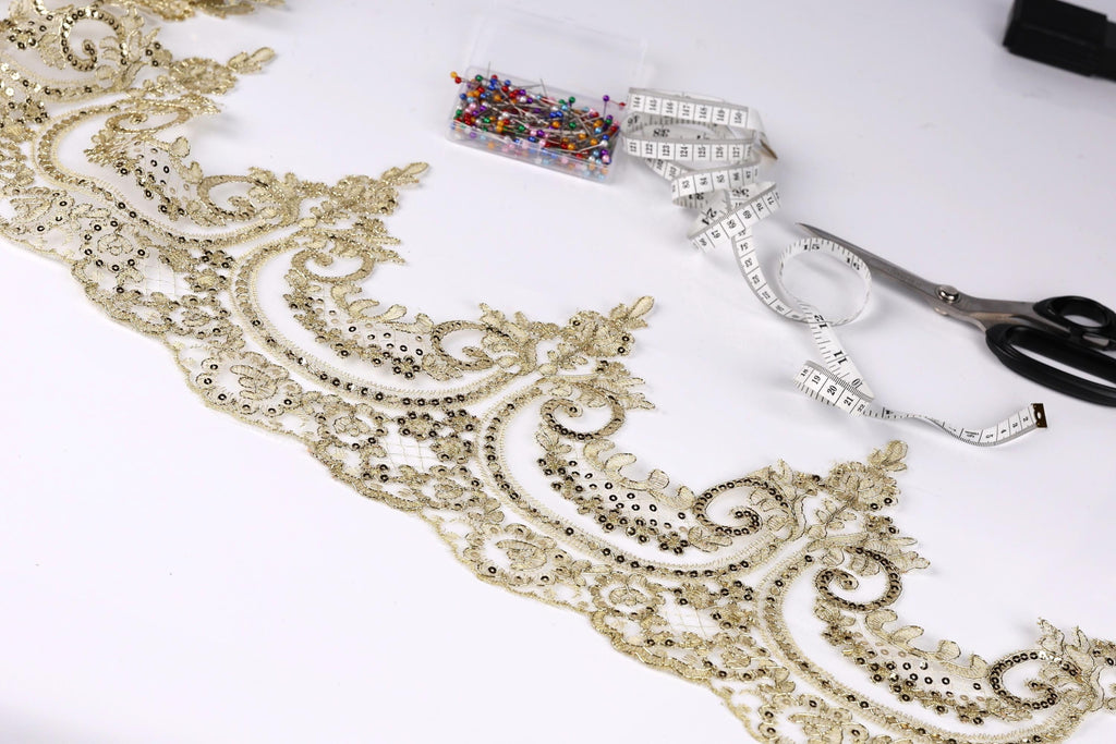 a close-up view of a decorative gold lace trim with intricate floral patterns, along with sewing tools such as scissors and a measuring tape.