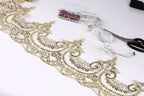 a close-up view of a decorative gold lace trim with intricate floral patterns, along with sewing tools such as scissors and a measuring tape.