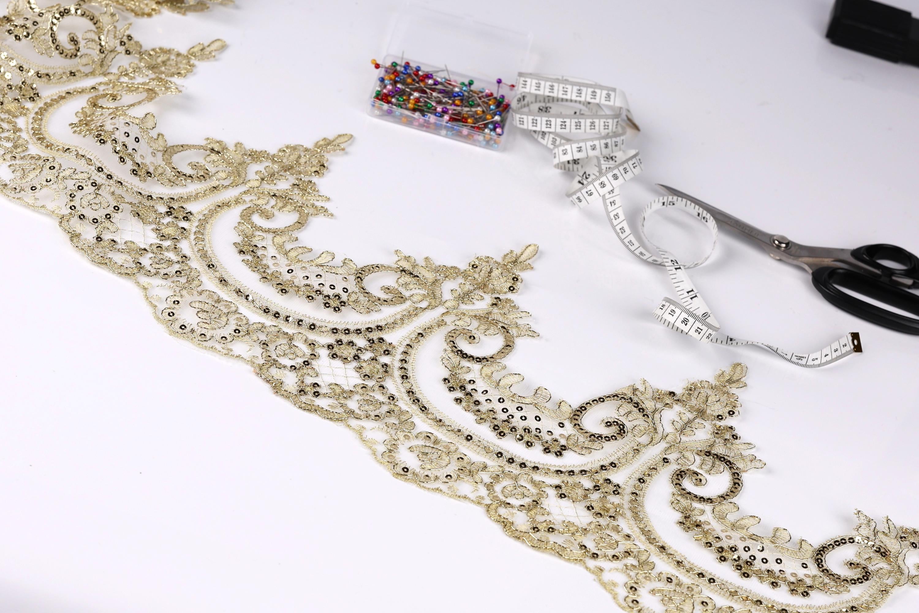 a close-up view of a decorative gold lace trim with intricate floral patterns, along with sewing tools such as scissors and a measuring tape.