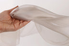 A hand is holding a piece of light gray fabric, which appears to be a sheer or sheer-like material.