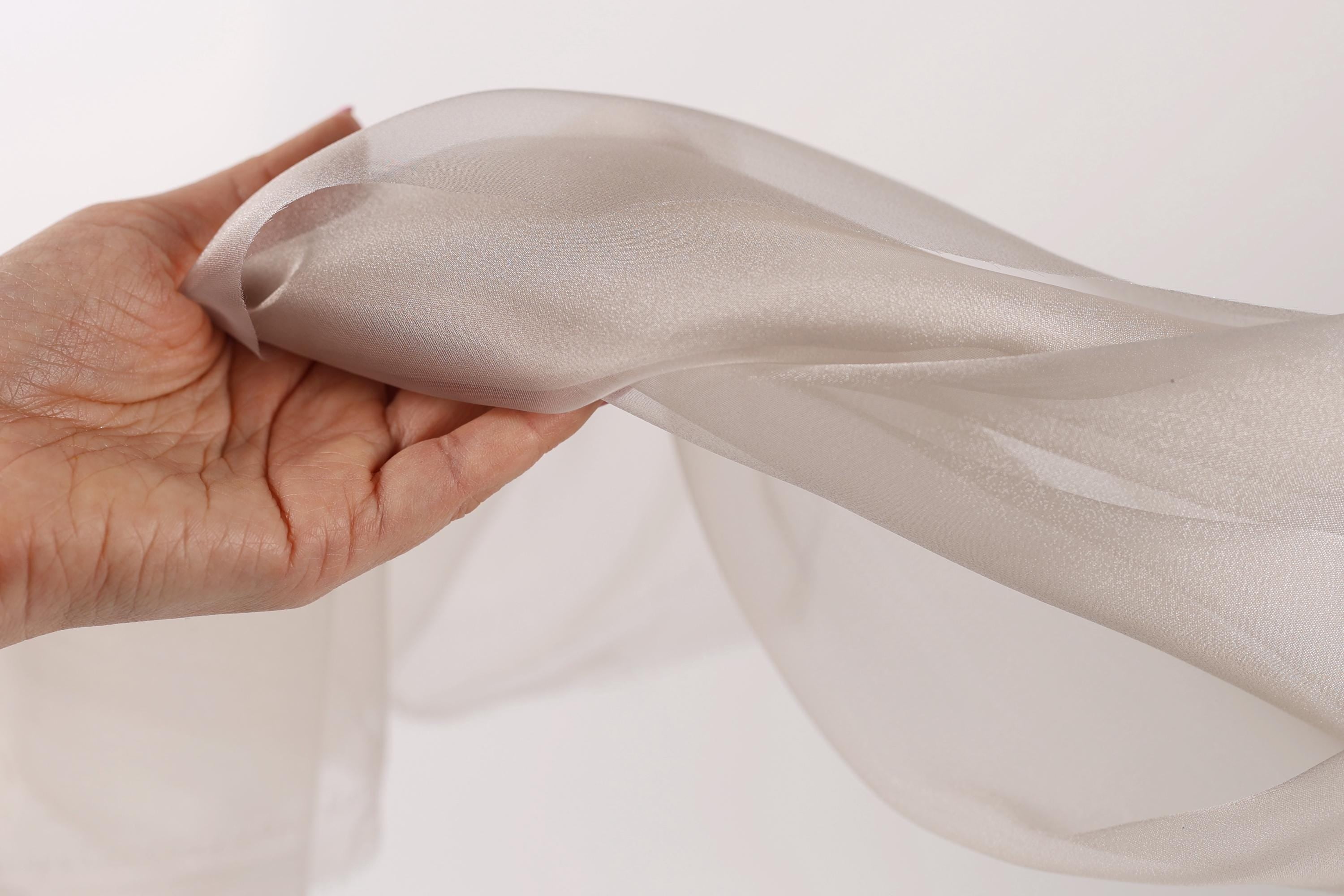 A hand is holding a piece of light gray fabric, which appears to be a sheer or sheer-like material.