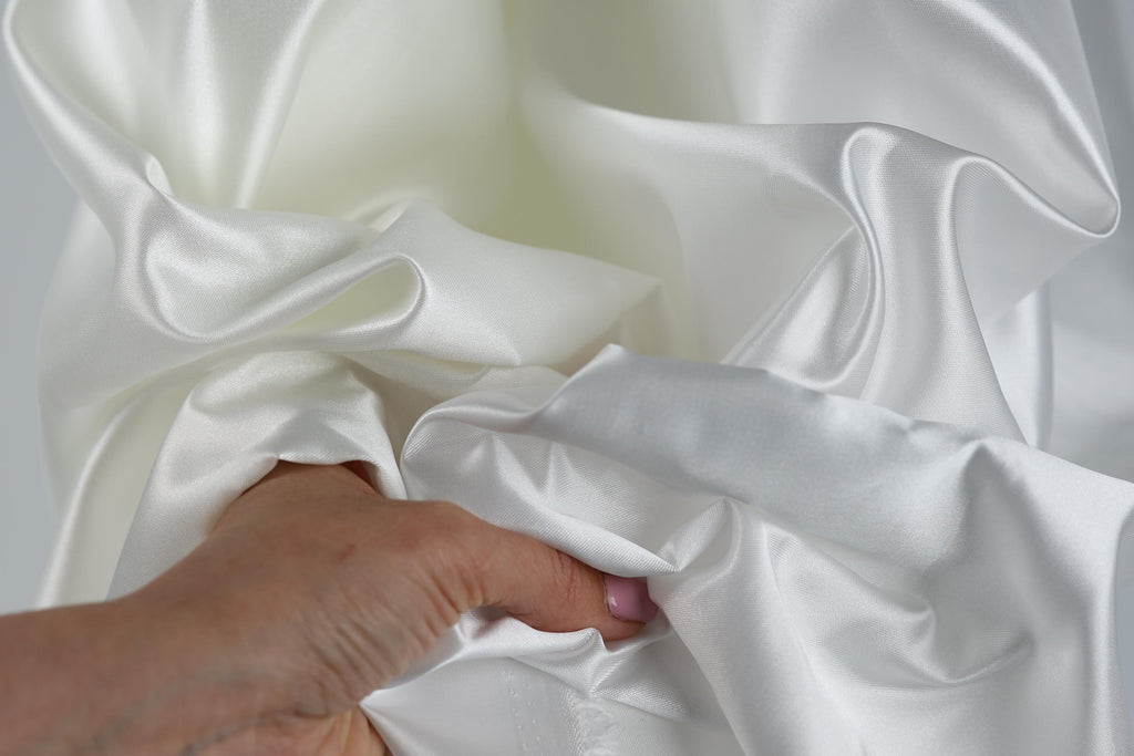 A hand is holding a piece of white satin fabric, with the fabric's folds and creases visible.