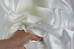 A hand is holding a piece of white satin fabric, with the fabric's folds and creases visible.