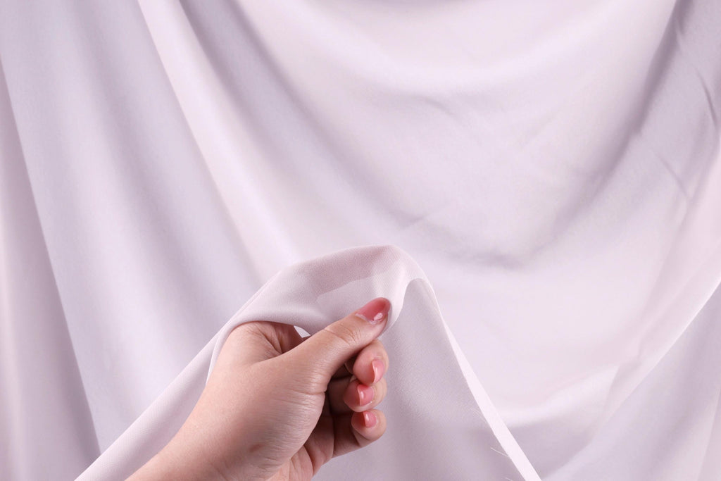 A hand holding a piece of white fabric against a blurred background.