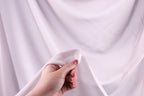 A hand holding a piece of white fabric against a blurred background.