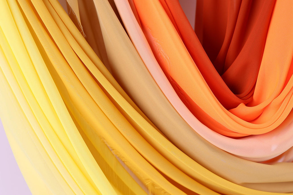 a close-up view of colorful fabric, with a mix of yellow, orange, and pink hues. The fabric appears to be folded or draped, creating a visually appealing and textured composition.