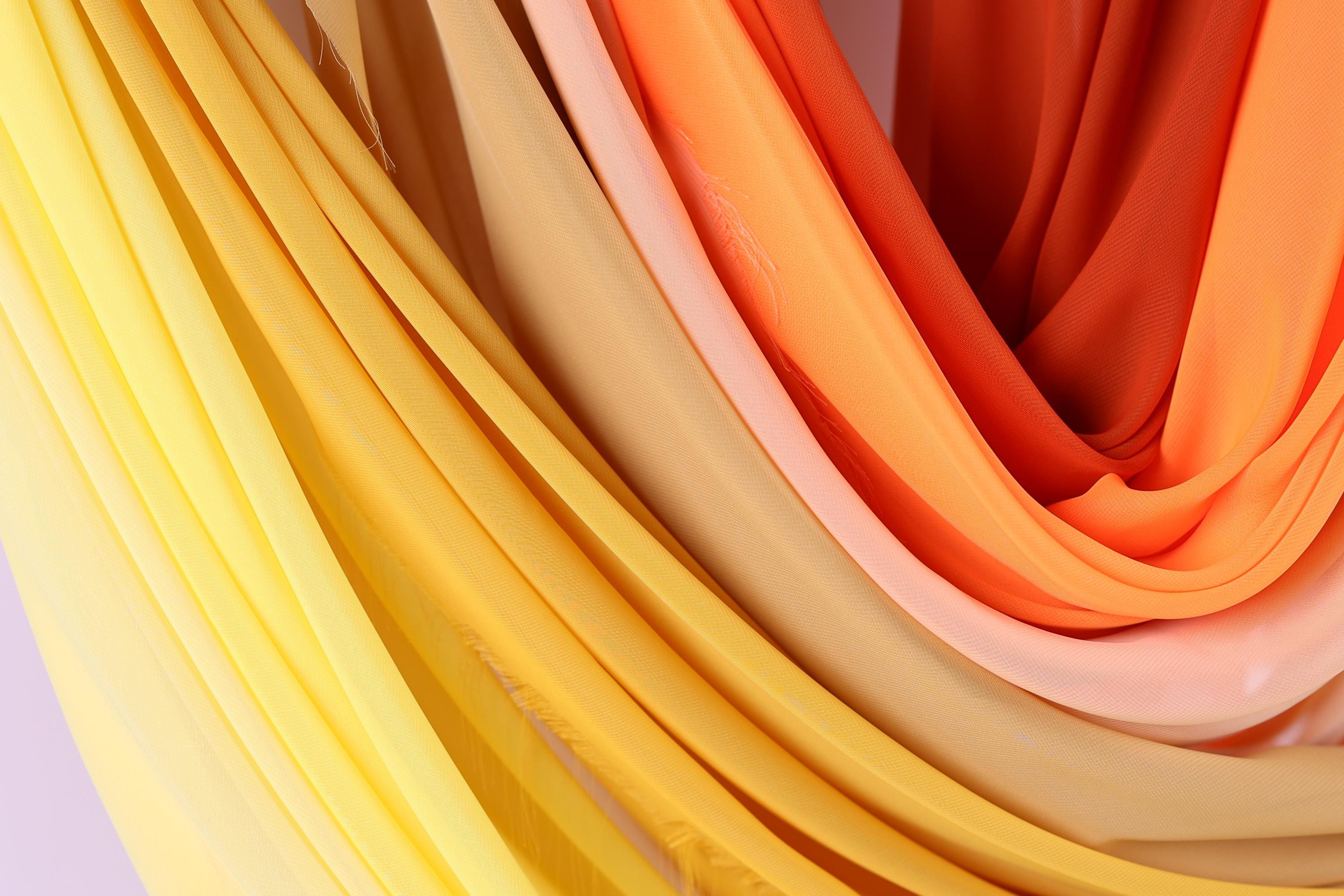 a close-up view of colorful fabric, with a mix of yellow, orange, and pink hues. The fabric appears to be folded or draped, creating a visually appealing and textured composition.