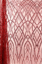 a close-up view of a fabric with a repeating pattern of red sequin designs. The pattern consists of various shapes and lines, creating a visually striking and intricate design. The fabric appears to be a pink background, which contrasts with the red sequin pattern and makes it stand out. The image does not contain any text or other objects, and the focus is solely on the fabric and its design.