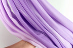 A close-up view of a hand holding a piece of purple fabric, with the fabric's folds and creases visible.