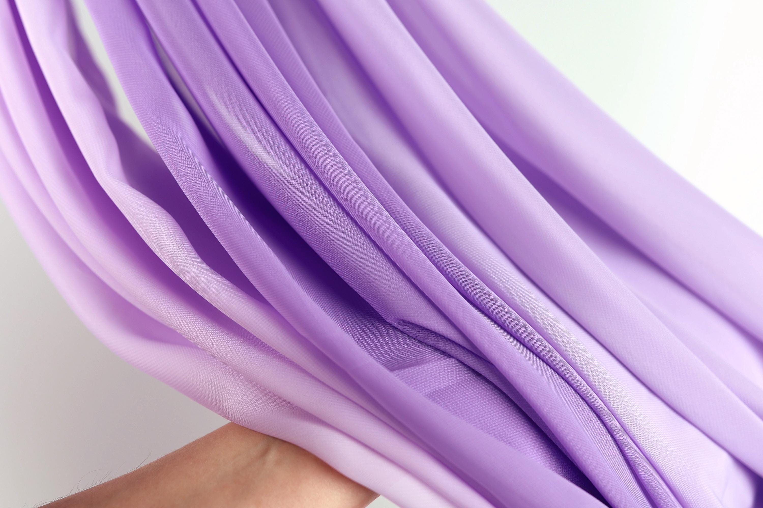 A close-up view of a hand holding a piece of purple fabric, with the fabric's folds and creases visible.