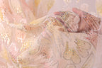 A close-up view of a delicate, hand-embroidered fabric with a floral pattern. The fabric appears to be made of sheer material, with a light pink and white color scheme. The intricate embroidery and beading on the fabric create a visually appealing and delicate appearance.