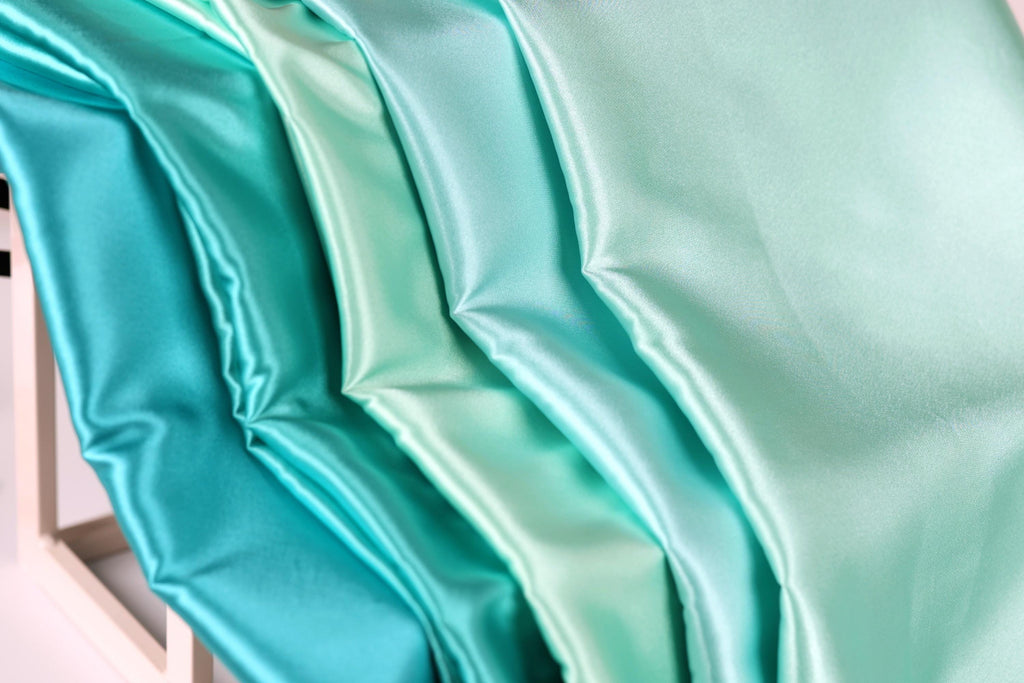 A close-up view of a fabric with a gradient of turquoise to mint colors, creating a visually appealing and vibrant pattern.