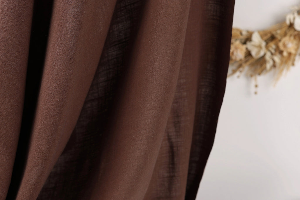a close-up view of a brown fabric, possibly a curtain or textile, with a blurred background that appears to be a wreath made of dried flowers.