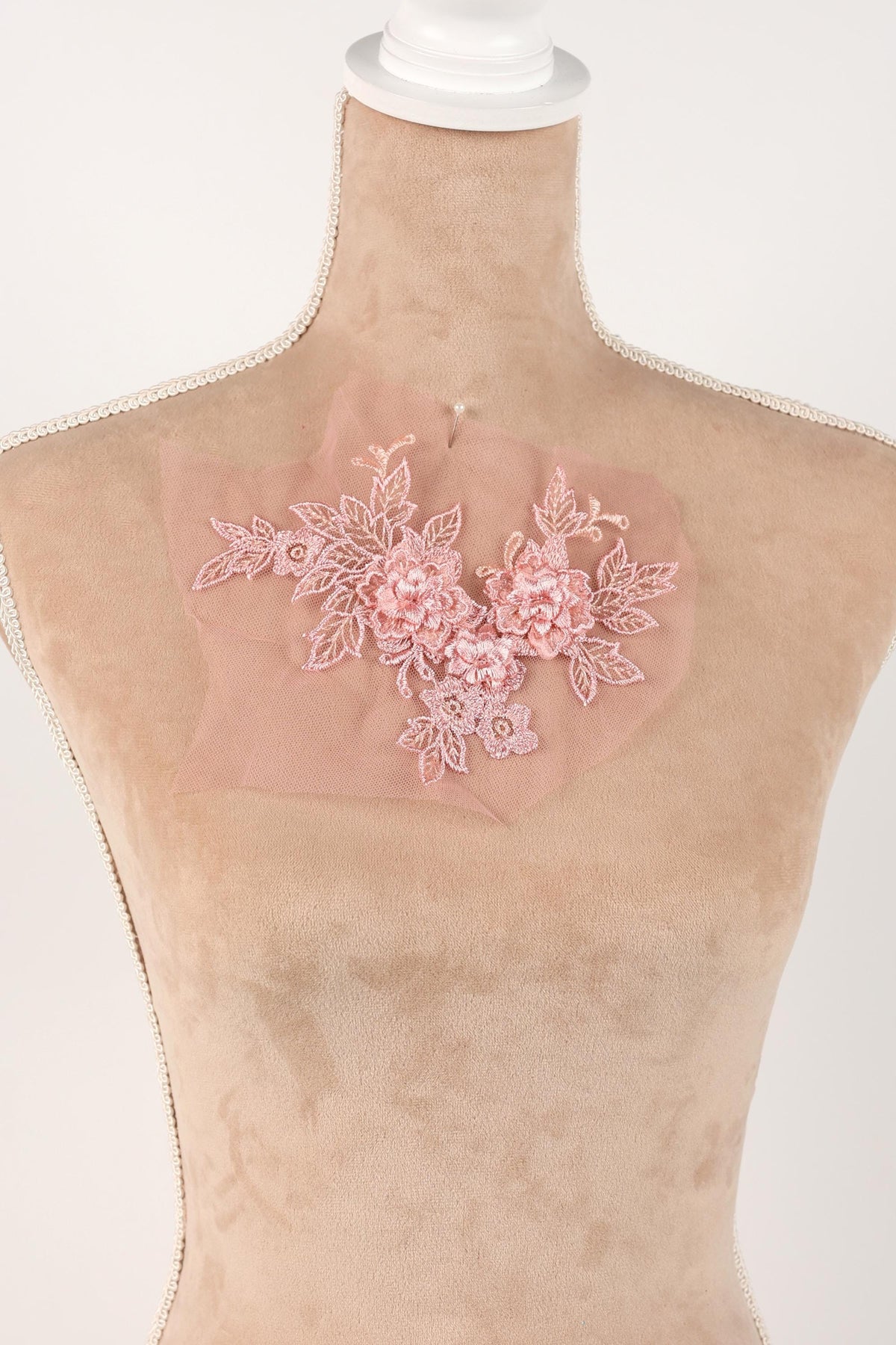 A mannequin wearing a pink floral lace piece on its chest.