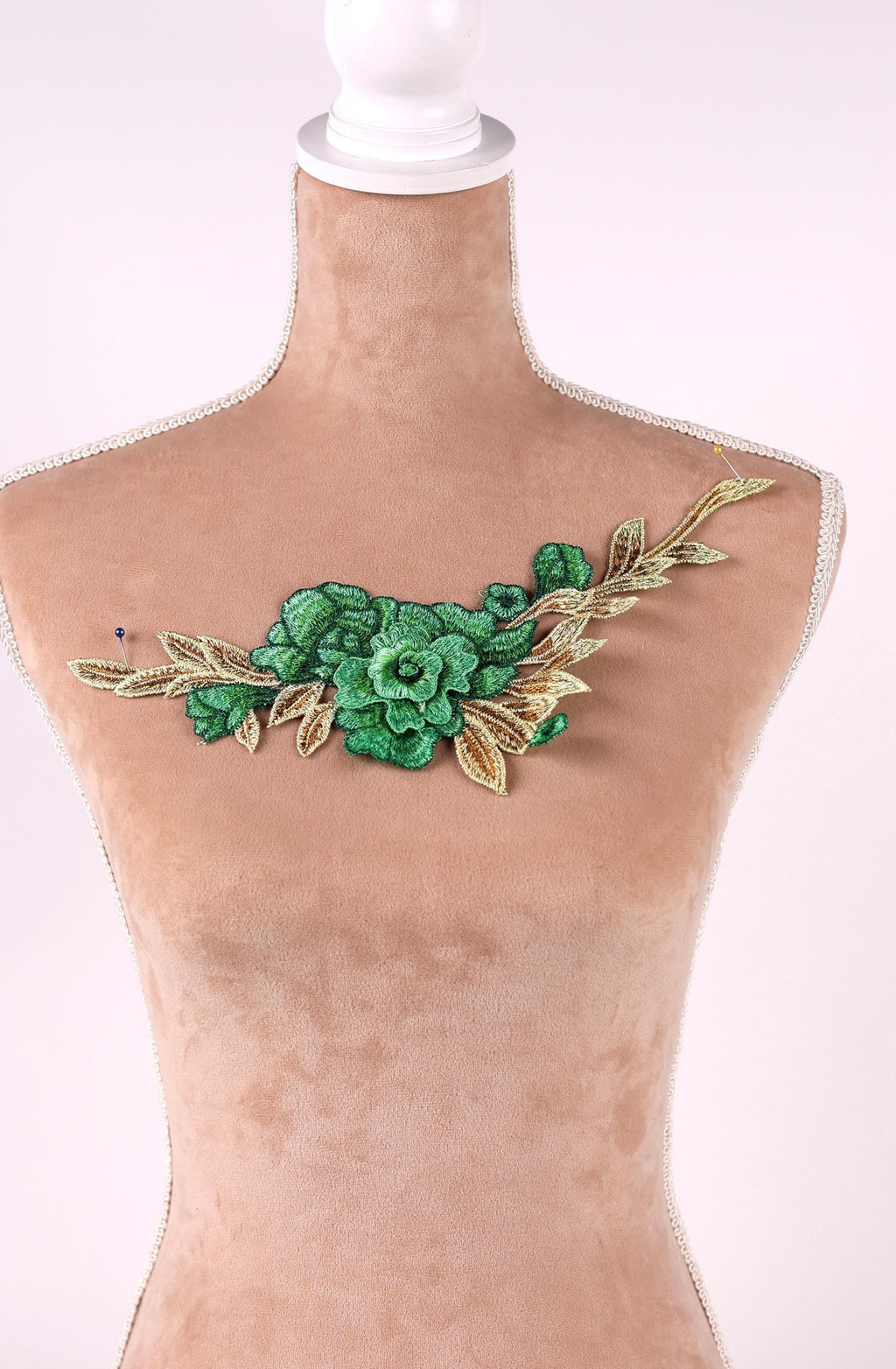 A mannequin wearing a beige dress with a green floral embroidered patch on the chest area.