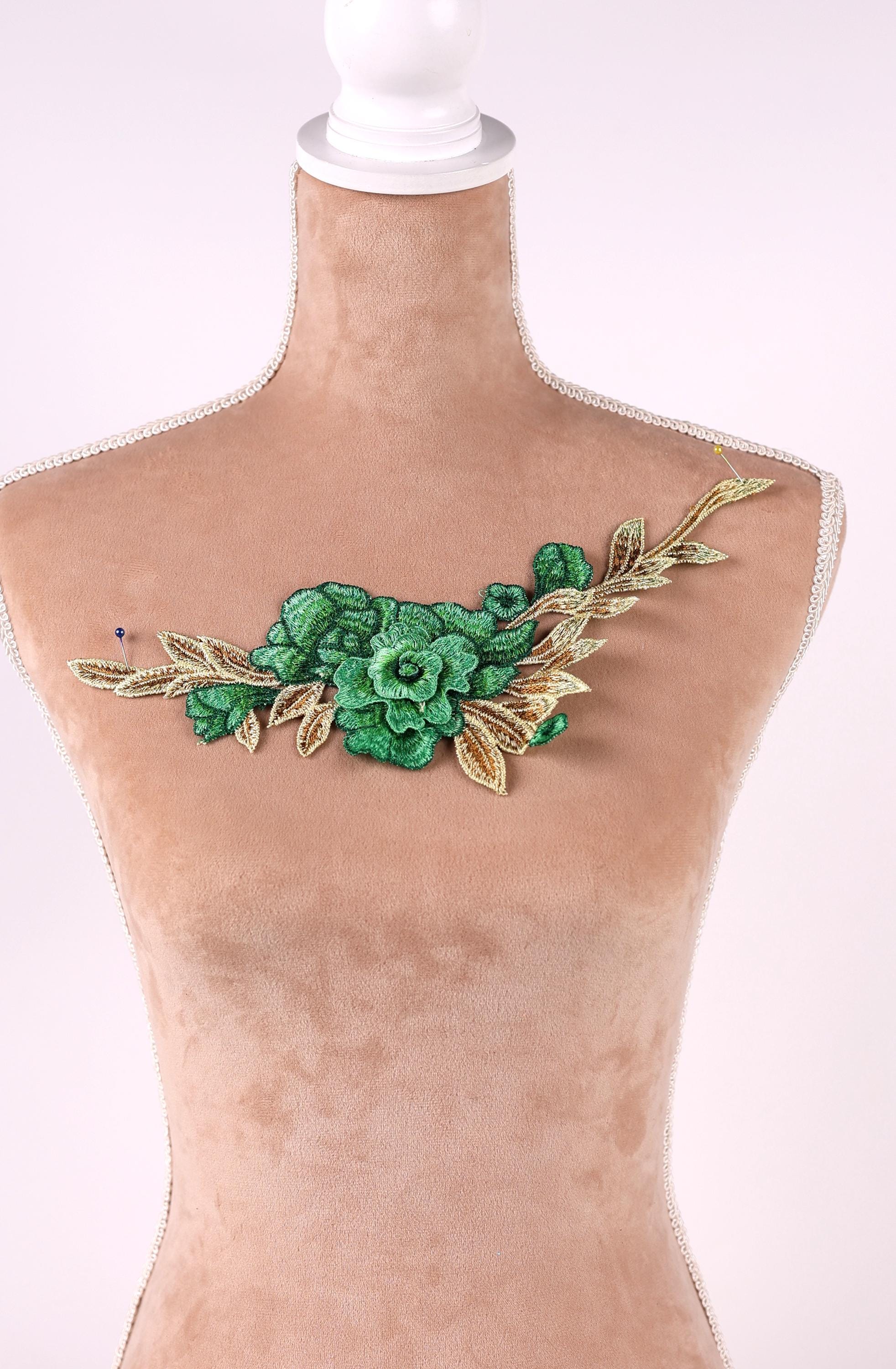 A mannequin wearing a beige dress with a green floral embroidered patch on the chest area.