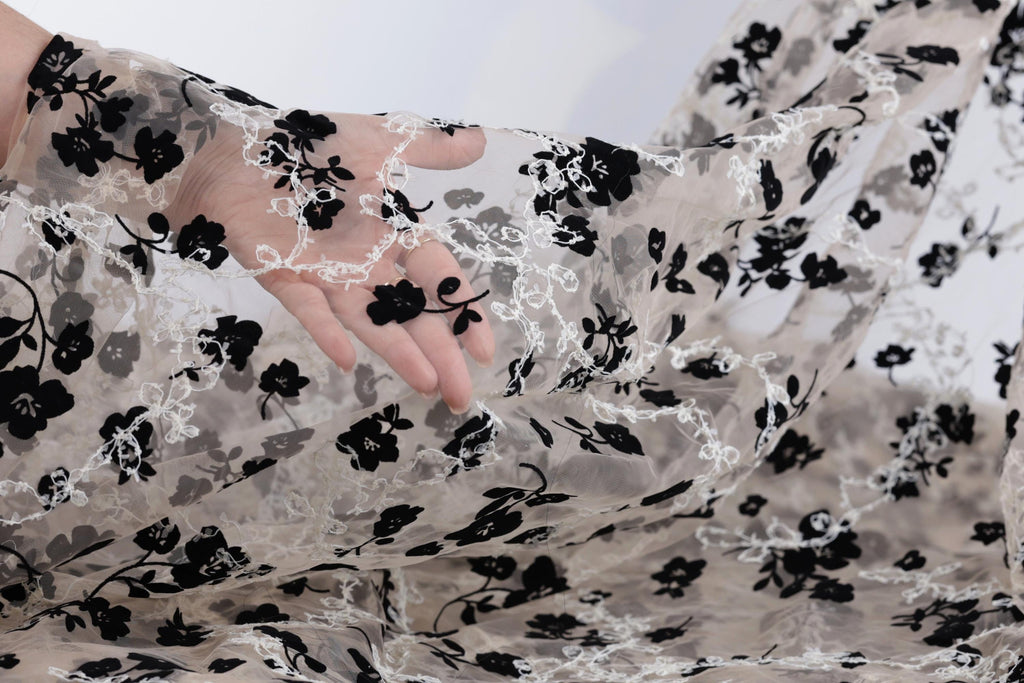 A hand is holding a piece of sheer fabric with a black and white floral pattern.