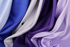 a close-up view of various colored satin fabrics, including blue, gray, and purple, arranged in a crumpled and flowing manner.
