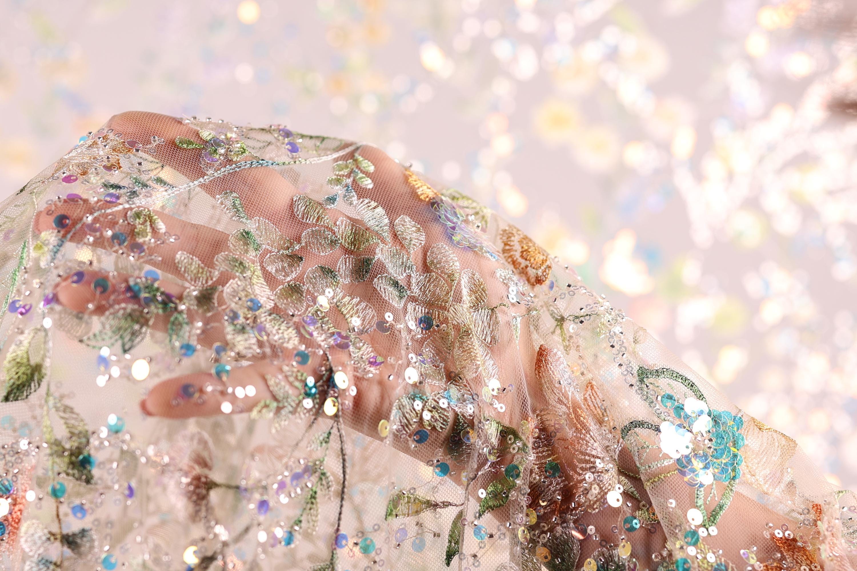 A close-up view of a hand holding a delicate, intricately embroidered fabric with a floral pattern.