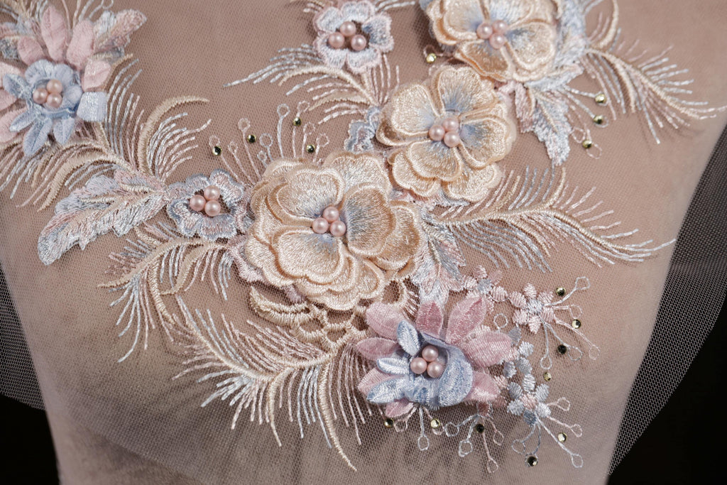 a close-up view of a delicate, intricate floral embroidery on a fabric. The embroidery is composed of various flowers and leaves, each meticulously crafted with small beads and pearls, creating a visually appealing and detailed design.