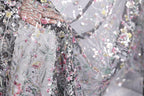 a close-up view of a delicate, intricately embroidered fabric with a floral pattern. The fabric appears to be a sheer material, with a variety of colors and designs, including pink, green, and white flowers. The image is a close-up of the fabric, showcasing the detailed embroidery and the intricate design elements.